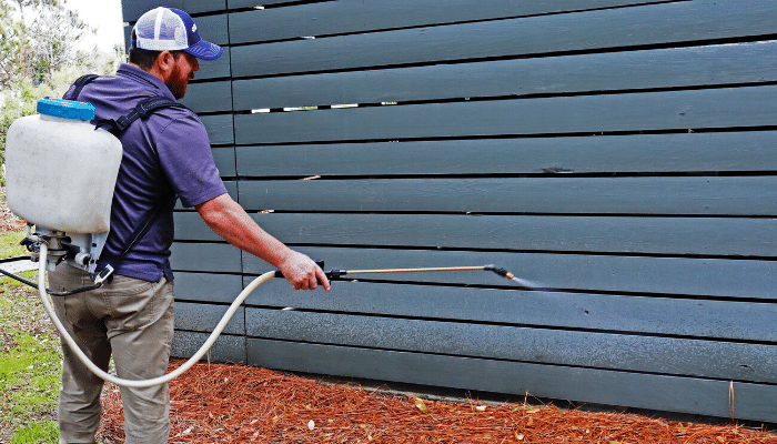 Person spraying pesticide along a wooden fence