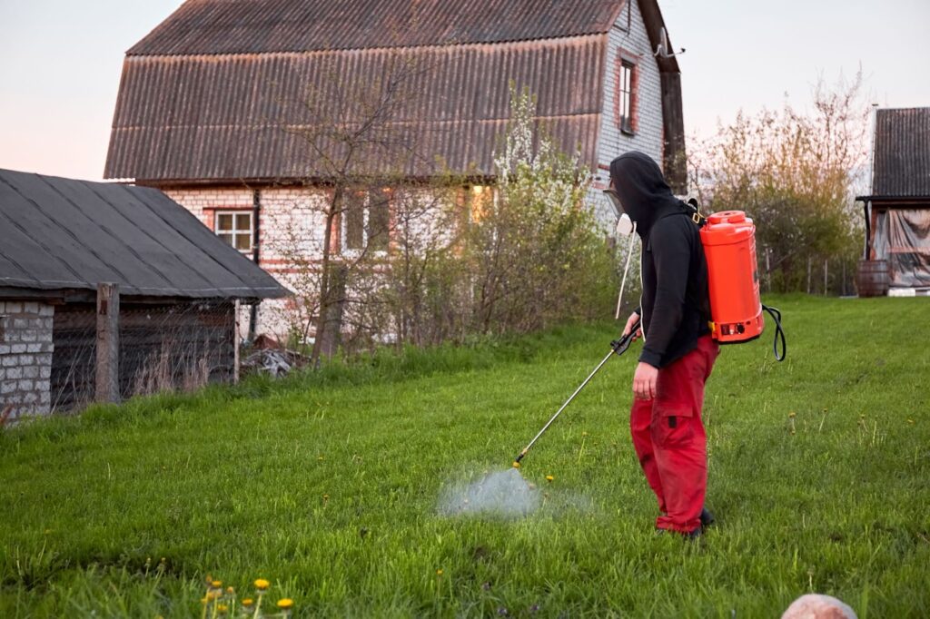 Man with backpack spraying lawn with hose for Lawn Service.