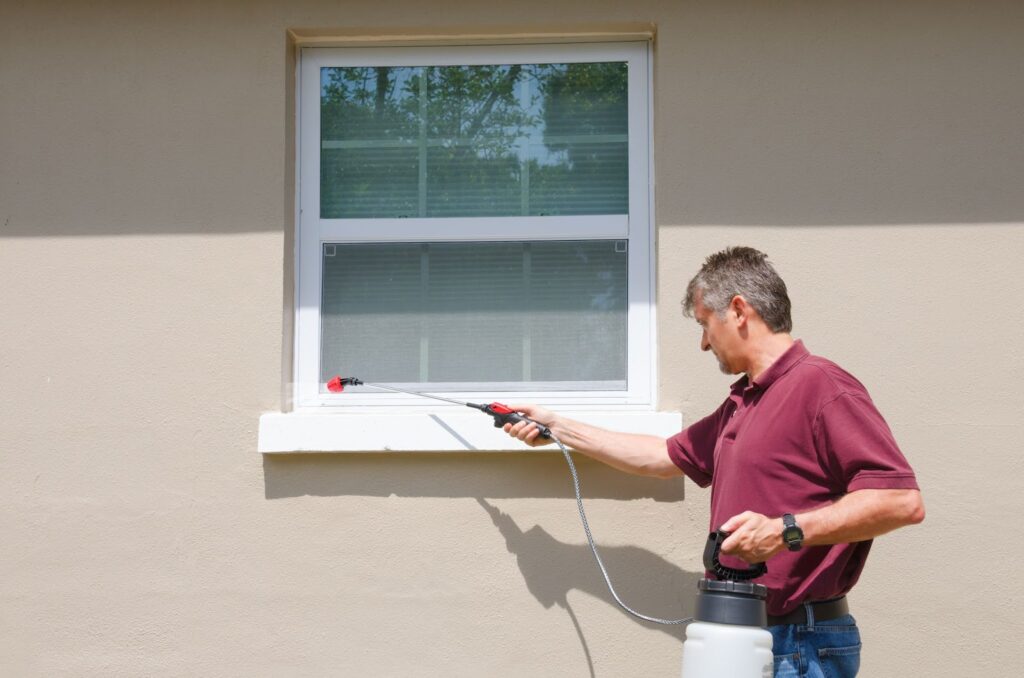 A man uses a sprayer to apply bug spray on a window, targeting pests effectively.