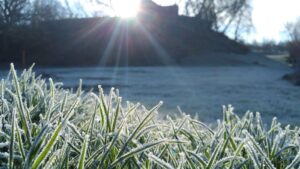 A layer of frost blankets the grass in front of a grand castle, highlighting the beauty of winter